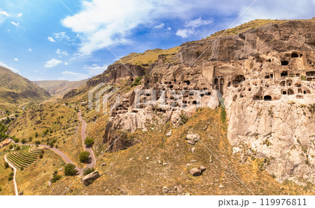 Aerial top view of Vardzia city on sunny summer day. Ancient cave monastery in Erusheti Mountain rocks at Kura River. Monument of medieval Georgian architecture, carved in rough rock. Georgia, Europe. Aerial top view of Vardzia city on sunny summer day. Ancient cave monastery in Erusheti Mountain rocks at Kura River. Monument of medieval Georgian architecture, carved in rough rock. Georgia, Europe. 119976811