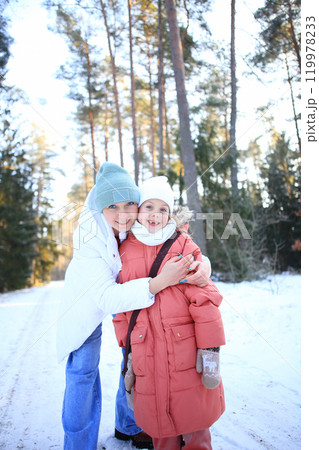 a mother lovingly embracing her children against the backdrop of a beautiful winter forest. a mother lovingly embracing her children against the backdrop of a beautiful winter forest. 119978233