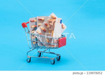 Pills and Capsules in Shopping Cart on Blue Background 119978852