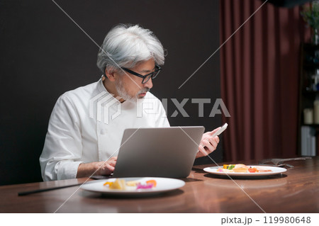 パソコンを見て料理の改良をするシェフ 119980648