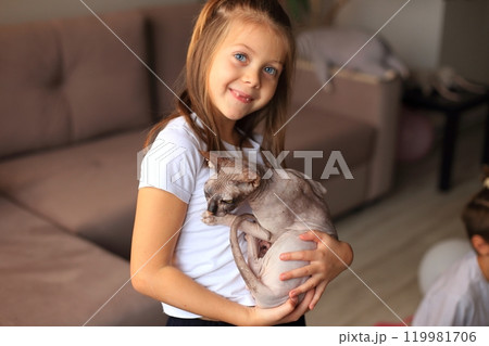 A joyful scene of a young girl playing with her adorable Sphynx cats. The unique, hairless cats are playfully interacting with her, creating a delightful atmosphere filled with laughter and affection. 119981706