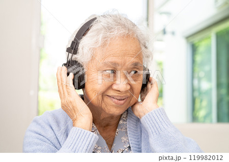 Asian senior woman listen to music with headphone smile and enjoy audio track in relaxing time. 119982012