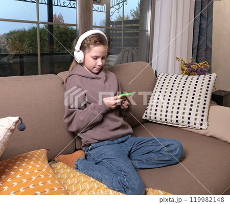 Joyful teenage girl wearing headphones with smartphone online. Pastime and Lifestyle. Joyful teenage girl wearing headphones with smartphone online. Pastime and Lifestyle. 119982148