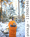 A young man stands in a winter forest, capturing the beauty of the snowy landscape with his smartphone. 119982446