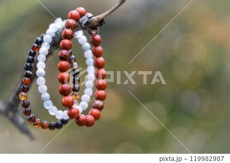 Red jasper and agate bracelets hang on a tree branch in autumn bokeh background, close-up. Red jasper and agate bracelets hang on a tree branch in autumn bokeh background, close-up. 119982987
