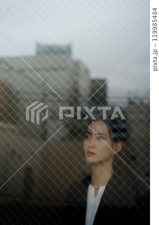 ガラス越しに写る街並みと物憂げな表情の若いスーツ女性 119985484