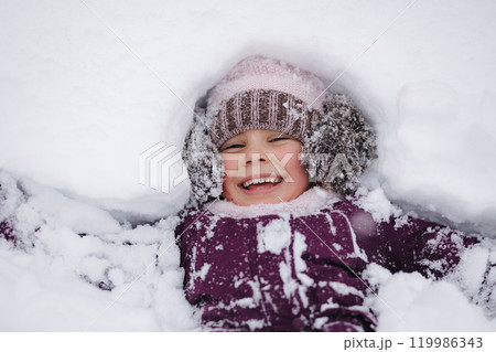 Little girl covered in snow, laughing and playing. A perfect scene of childhood excitement in a winter wonderland 119986343