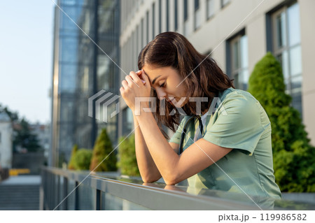 Young female doctor standing near clinic and feeling tired Young female doctor standing near clinic and feeling tired 119986582