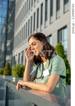 Young female doctor standing near clinic and feeling tired Young female doctor standing near clinic and feeling tired 119986583