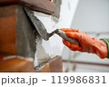 A person is using a trowel to apply cement to a wall. 119986831