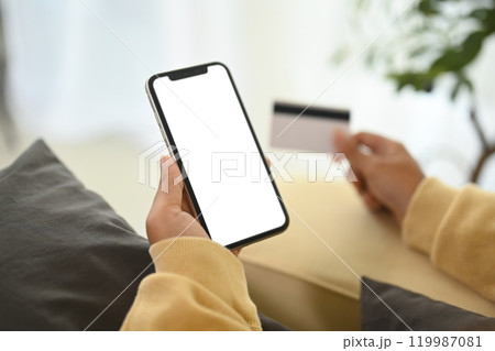 Close up woman making an online purchase with credit card and smartphone 119987081