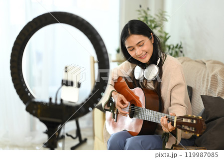 Smiling female music influencer recording video tutorial on playing guitar Smiling female music influencer recording video tutorial on playing guitar 119987085