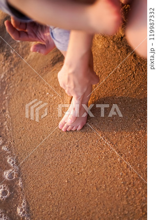 The joyful picture of the baby first step footprint on the glittering sand at the beach with the parents filled with love and kindness. The air bubble of the seawater. Mother hand on child foot 119987332