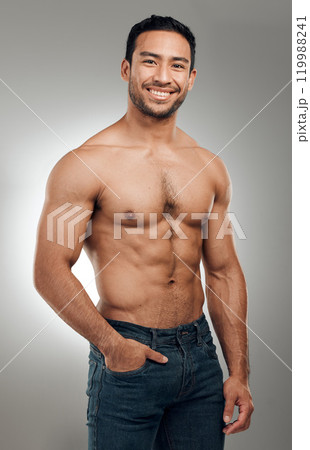 Man, portrait and smiling in studio with abs or muscles, shirtless and grey background with model or bodybuilder. Jeans, strong chest and Asian male person on backdrop, confidence with six pack 119988241