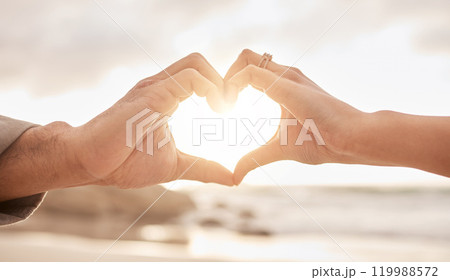Couple, hands and heart by sunset with love on beach for honeymoon or vacation in summer with romantic gesture. Commitment, partnership and marriage with trust, promise and together in the Maldives. 119988572