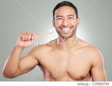 Portrait, happy man and brushing teeth in studio for dental hygiene, wellness or oral health. Face, toothpaste or cleaning with natural bamboo toothbrush for orthodontics isolated on gray background 119988740