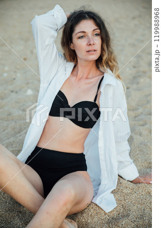 Portrait of a beautiful woman in a black swimsuit on the beach by the sea Portrait of a beautiful woman in a black swimsuit on the beach by the sea 119988968