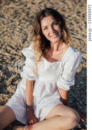 Beautiful slim fashionable woman in white summer dress on the beach by the sea 119988972