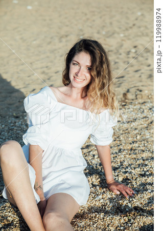 Beautiful slim fashionable woman in white summer dress on the beach by the sea 119988974