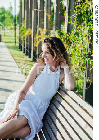 woman in light summer dress smiling in park on walk 119988975