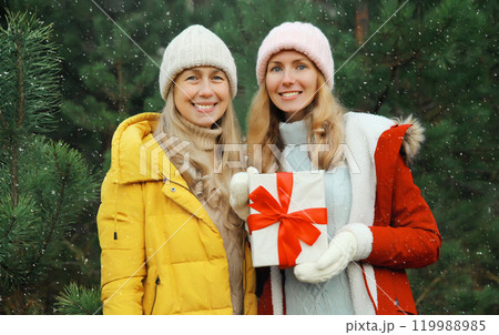 Happy smiling women friends, gift box, celebration on Christmas tree background in winter forest 119988985