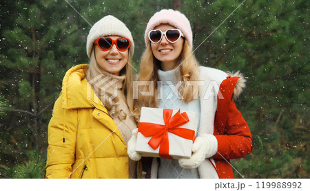 Happy smiling women friends, gift box, celebration on Christmas tree background in winter forest 119988992