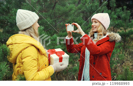 Happy smiling women friends, gift box, celebration on Christmas tree background in winter forest 119988993