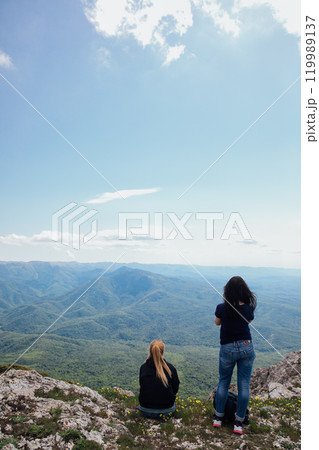 Two female traveler looking at the view from the top of the mountain on a hike Two female traveler looking at the view from the top of the mountain on a hike 119989137
