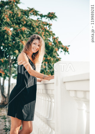Beautiful fashionable woman in a black summer dress walking around the city 119989281