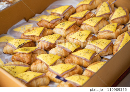 Appetizing croissant ham and cheese sandwiches in a paper box, enhanced with oregano spray. 119989356