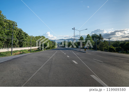 A ground-level perspective of a rural street in Tak Province, Thailand, in open sky during the day. This road serves as key transportation artery to western region of country. A ground-level perspective of a rural street in Tak Province, Thailand, in open sky during the day. This road serves as key transportation artery to western region of country. 119989380