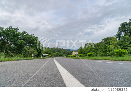 A ground-level perspective of a rural street in Tak Province, Thailand, in open sky during the day. This road serves as key transportation artery to western region of country. 119989381