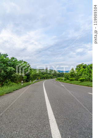 A ground-level perspective of a rural street in Tak Province, Thailand, in open sky during the day. This road serves as key transportation artery to western region of country. 119989384