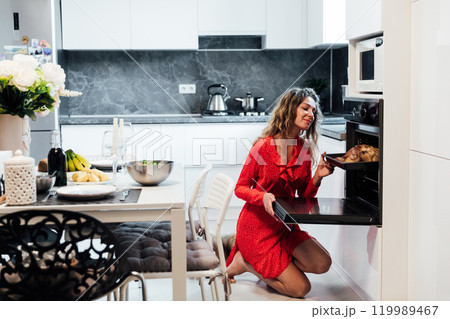 Woman in red dress cooking a romantic dinner in the kitchen Woman in red dress cooking a romantic dinner in the kitchen 119989467