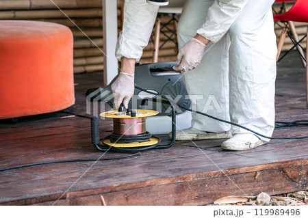 Professional technical man in prevention suit with his sterilizing machine and disinfecting water sprays in the outdoor field for purifying coronavirus (COVID-19). 119989496