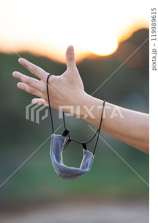 Close up to textile fabric mask is hanged on to man arm with the twilight background. Close up to textile fabric mask is hanged on to man arm with the twilight background. 119989615