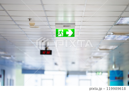 Green White light neon sign depicting a fire exit with interior mirror door background. It hung on ceiling. 119989618
