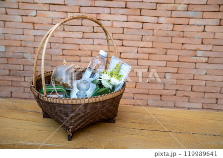 The Stuffs in a wicker basket for offer food or give alms to the monks on a wooden chair with the brick wall background. The Stuffs in a wicker basket for offer food or give alms to the monks on a wooden chair with the brick wall background. 119989641