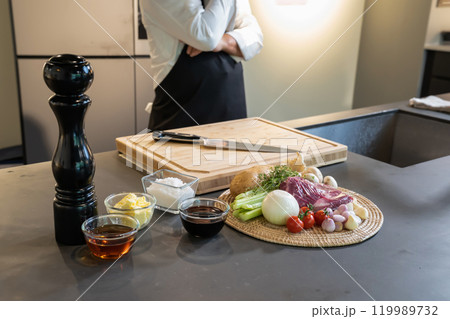 Environment on counter kitchen, prepared Onion, Beef, Sauce and food ingredients for Steak Cooking with standing professional chef background behind it. Environment on counter kitchen, prepared Onion, Beef, Sauce and food ingredients for Steak Cooking with standing professional chef background behind it. 119989732
