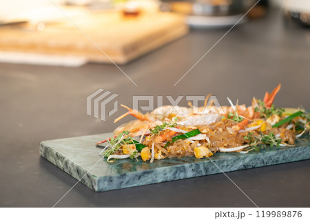 Close up to the Lobster Pad Thai is ready to serve with fried noodle, tofu and other ingredients on a rectangular plate in studio light. Close up to the Lobster Pad Thai is ready to serve with fried noodle, tofu and other ingredients on a rectangular plate in studio light. 119989876