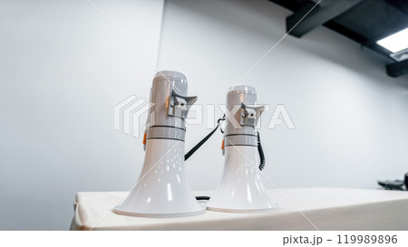 Two white - gray MEGAPHONE are laid on cream table in empty hall, ready to used for event corona virus vaccine booster in Bangkok, Thailand. 119989896