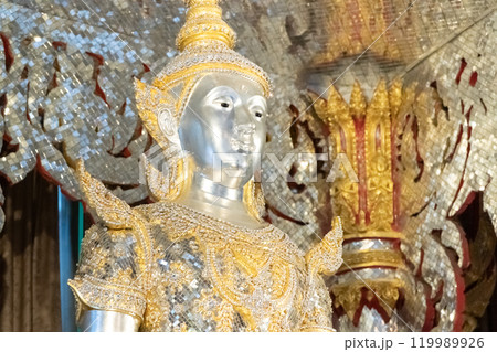 Deity statue standing straight made of silver, wearing silver gold costume with Chada on top of his head. Surrounded by sparkleling decoration. Deity statue standing straight made of silver, wearing silver gold costume with Chada on top of his head. Surrounded by sparkleling decoration. 119989926
