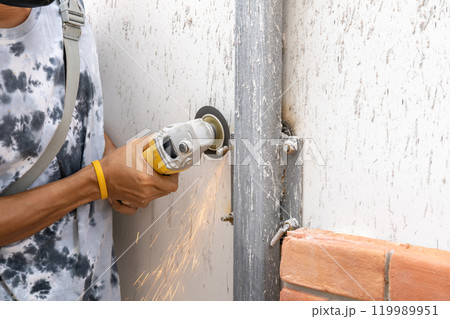 Asian worker young man sawing and kept detailed metal screw from a steel pole for preparing to install foam brick wall. 119989951
