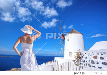 Beautiful young woman enjoying the view of Oia village with windmill on Santorini island in Greece 119991126