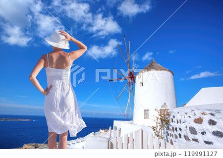 Beautiful young woman enjoying the view of Oia village with windmill on Santorini island in Greece Beautiful young woman enjoying the view of Oia village with windmill on Santorini island in Greece 119991127
