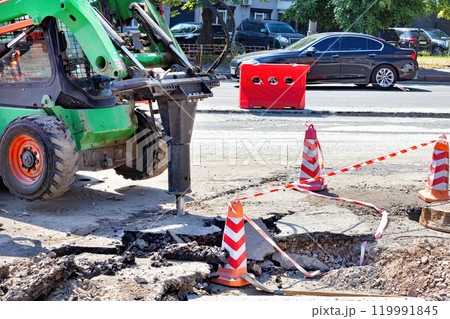 Construction work in progress on a city street with machinery and safety barriers in bright sunlight Construction work in progress on a city street with machinery and safety barriers in bright sunlight 119991845
