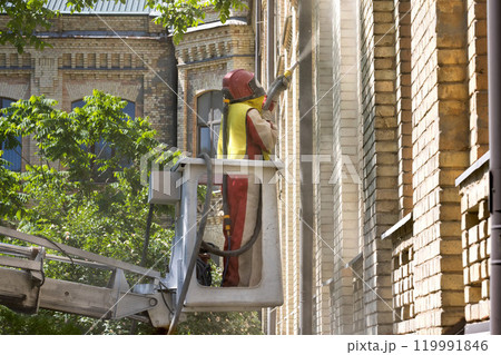 Worker using a lift to clean the exterior walls of a historic building under a clear blue sky Worker using a lift to clean the exterior walls of a historic building under a clear blue sky 119991846