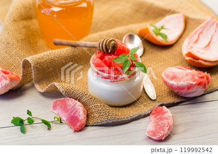 homemade sweet yogurt in a glass jar with pieces of red ripe grapefruit and honey, on a wooden table 119992542