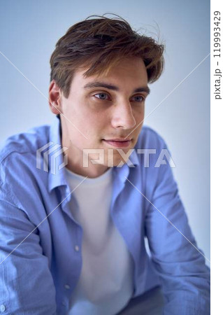 portrait of a handsome young adult man in a blue shirt sitting on a chair on a blue background portrait of a handsome young adult man in a blue shirt sitting on a chair on a blue background 119993429