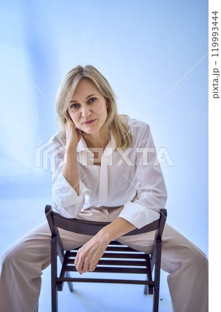 portrait of a stylish blonde middle-aged woman in a white blouse and beige pants portrait of a stylish blonde middle-aged woman in a white blouse and beige pants 119993444